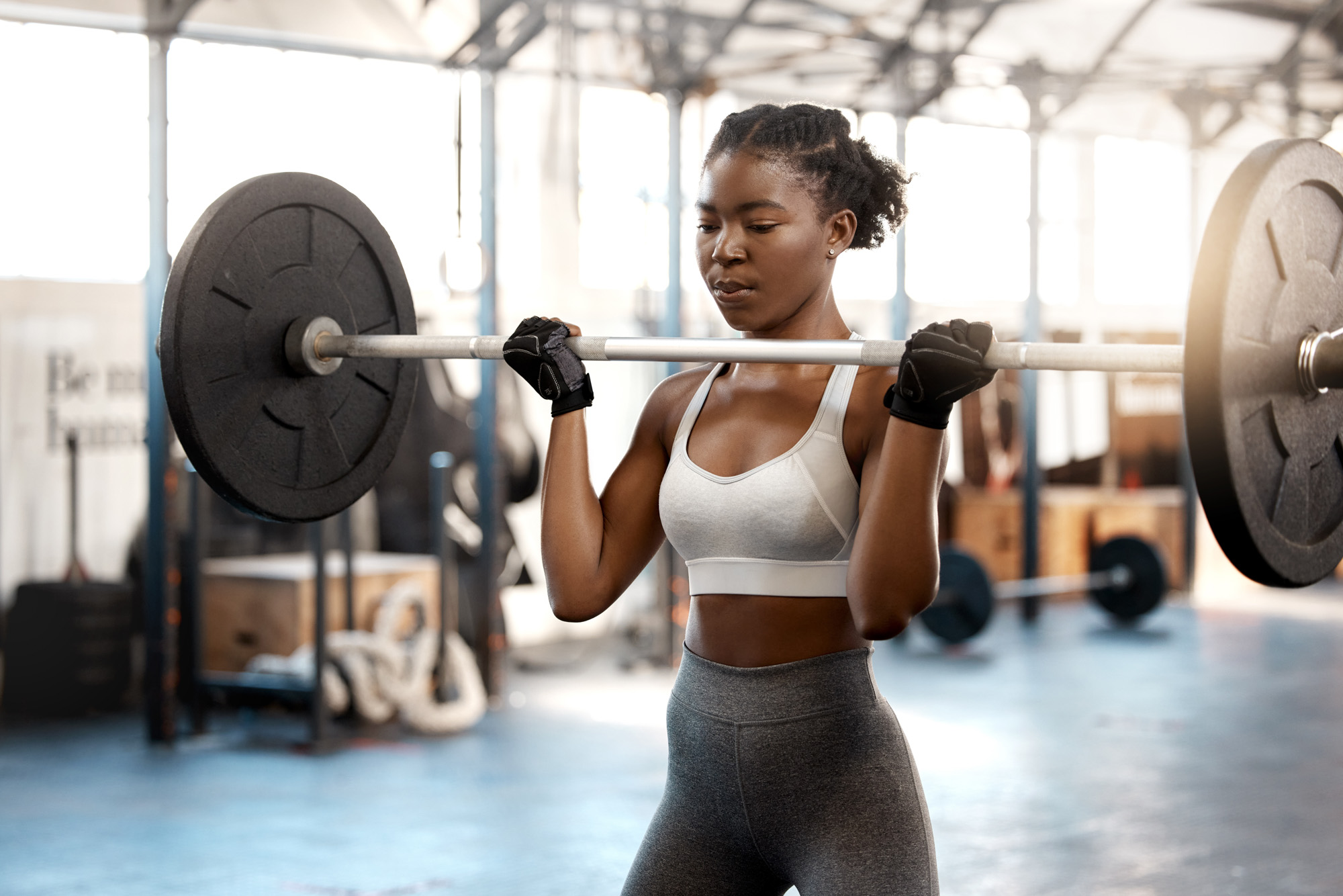 A fit woman wearing gym clothes lifts a heavy barbell in a gym