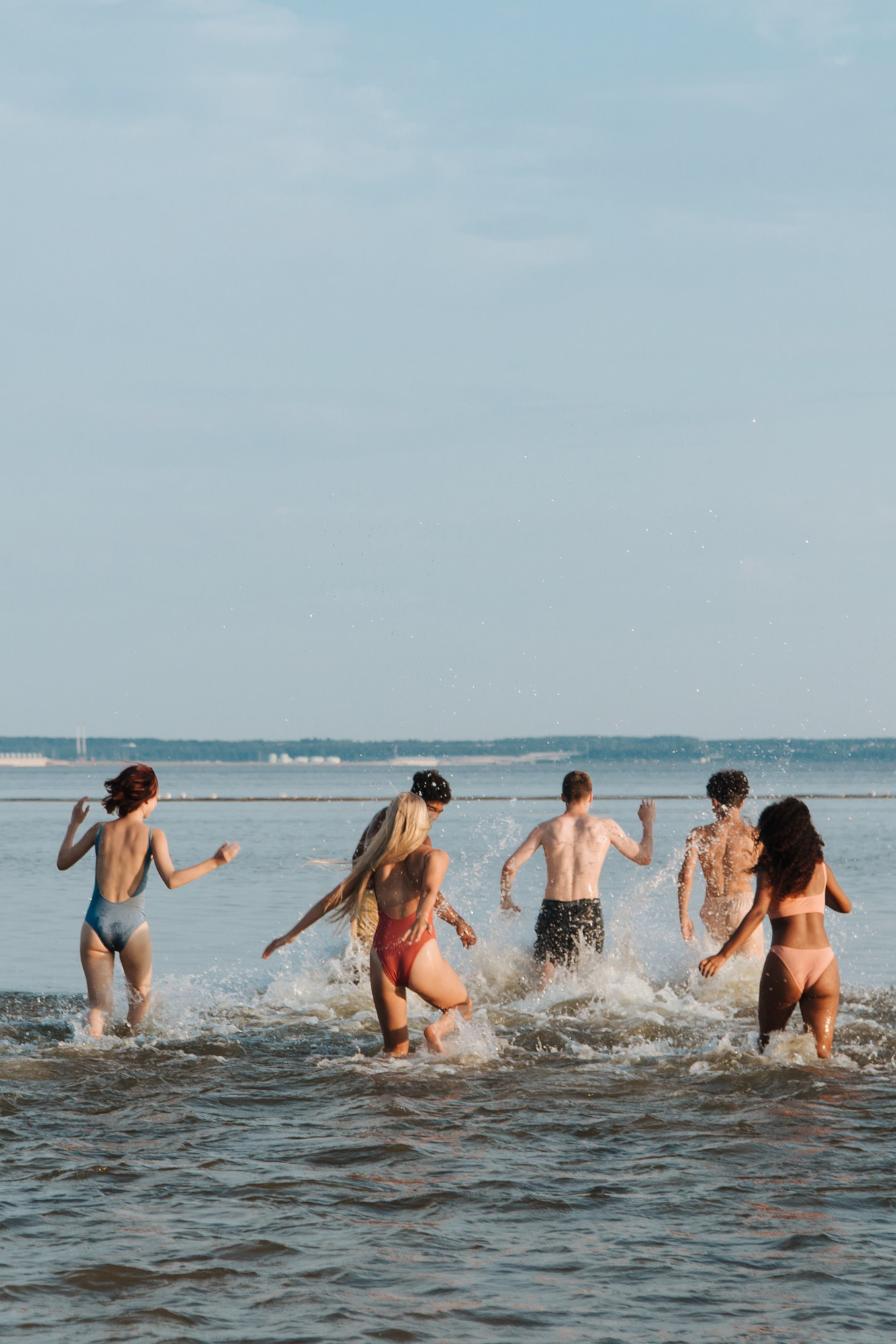 A group of friends running into the ocean water creating a splash