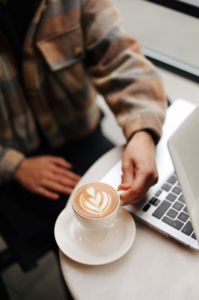 A person in a plaid shirt with a latte next to a laptop in cafe