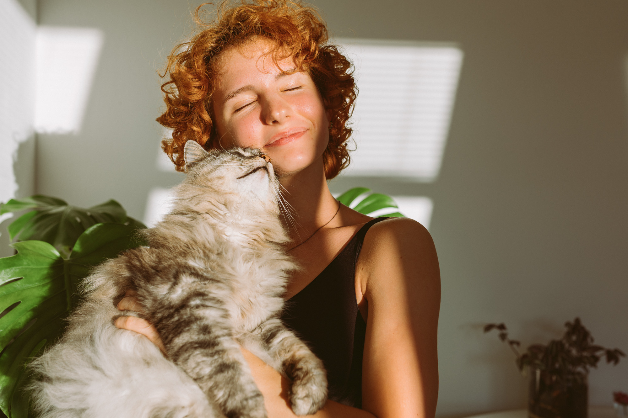 A young woman with curly red hair lovingly hugging a fluffy tabby cat