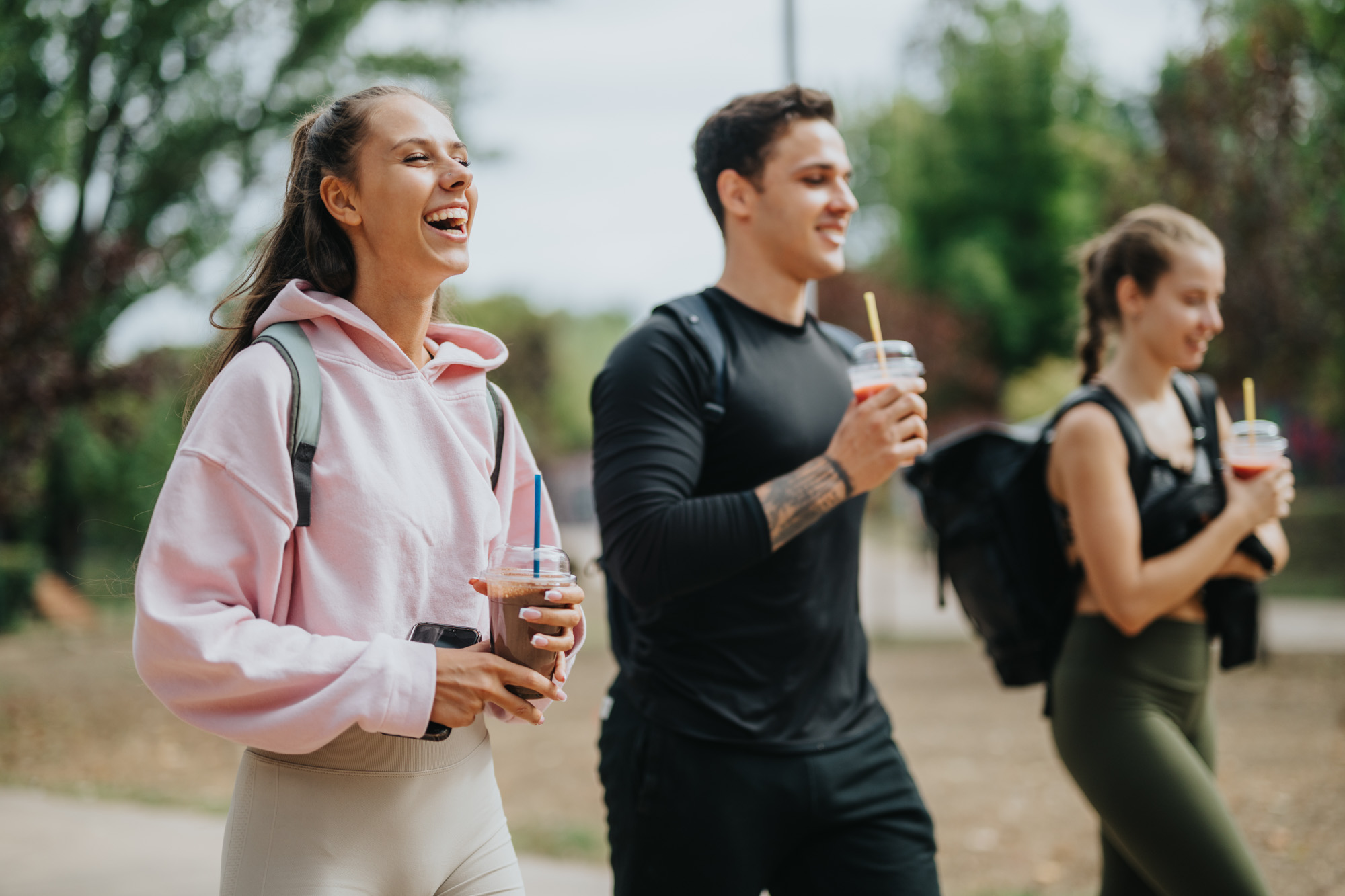 Three friends walk together in a park holding drinks