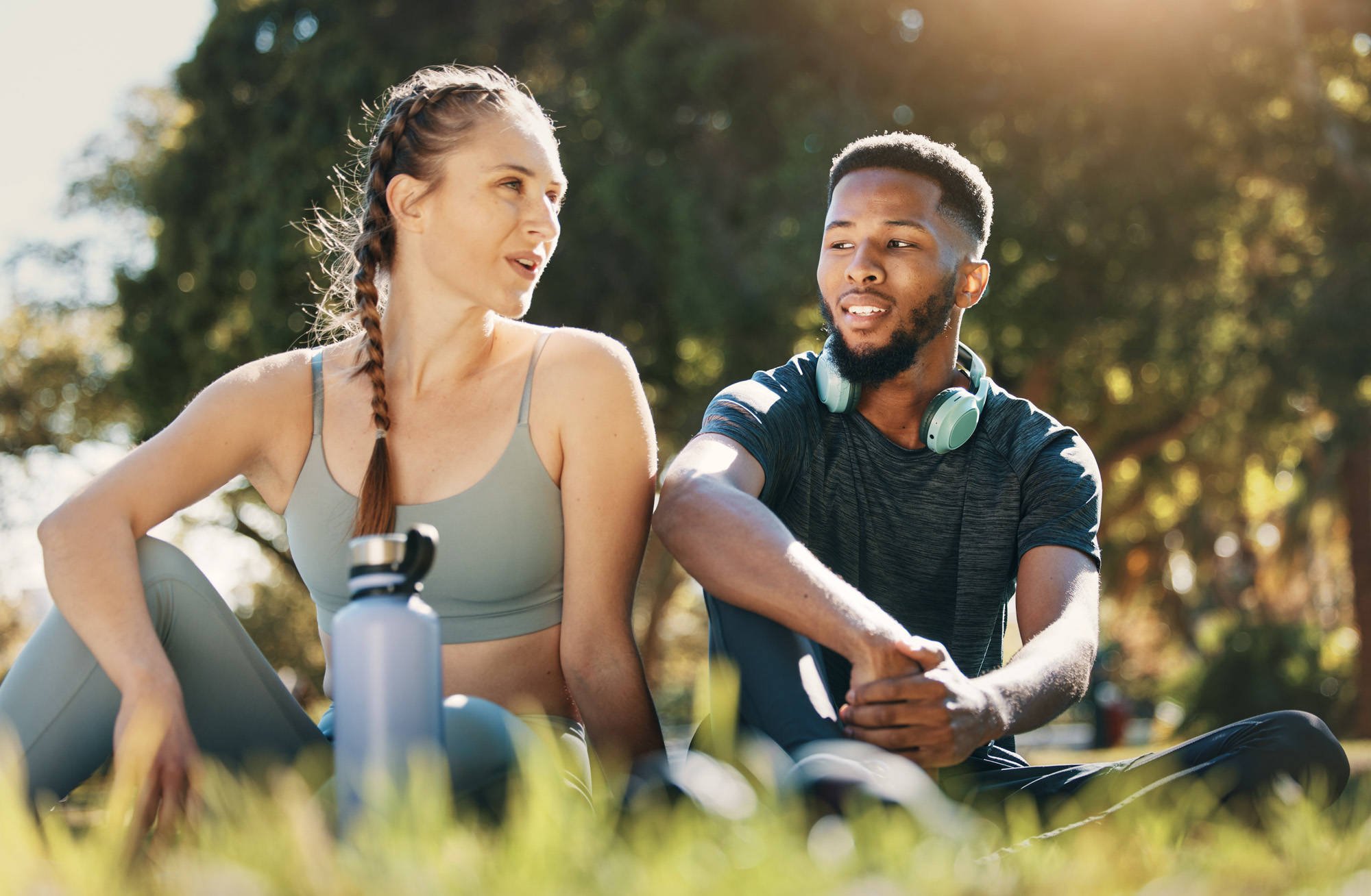 Two fit people talking while resting on the grass after an outdoor workout
