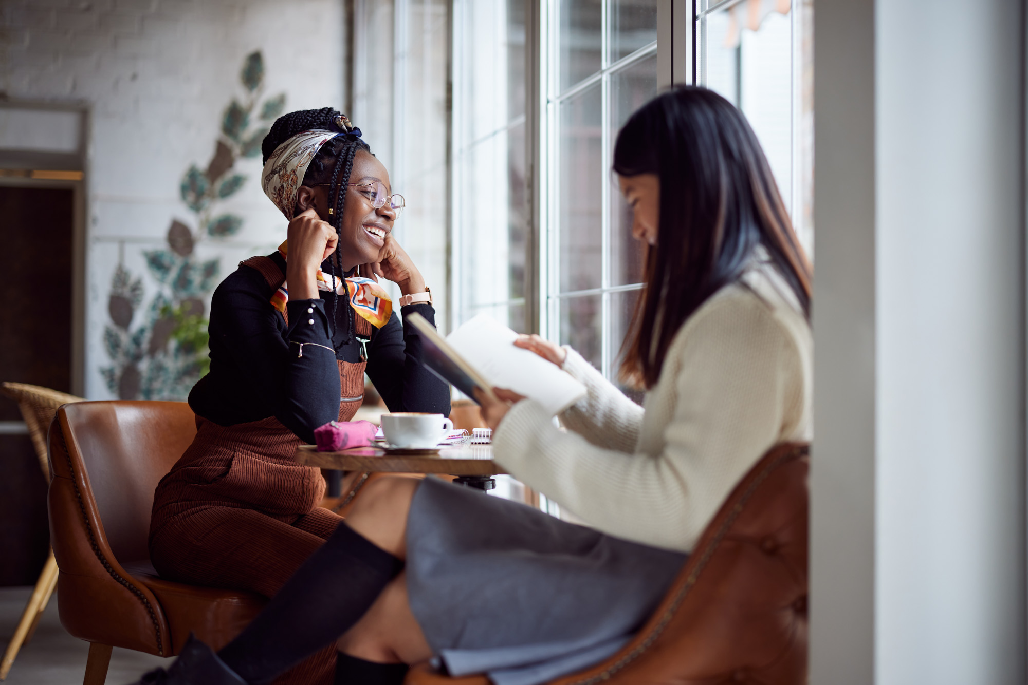 Two women sitting at a cafe table smiling while studying together